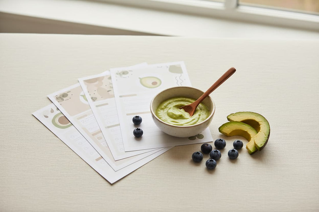 Printed baby feeding guides and checklists arranged on a cream linen surface with a wooden spoon, small bowl of purée, and fresh fruit — illustrating the Baby Food Starter Guide printable kit
